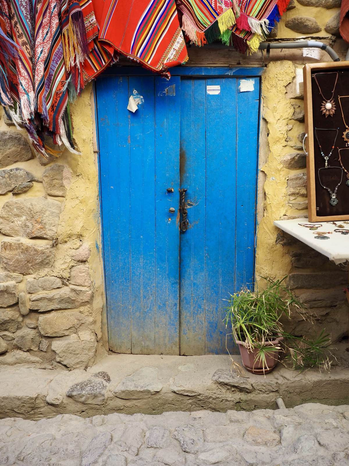 A bright blue wooden door beneath hanging woven textiles