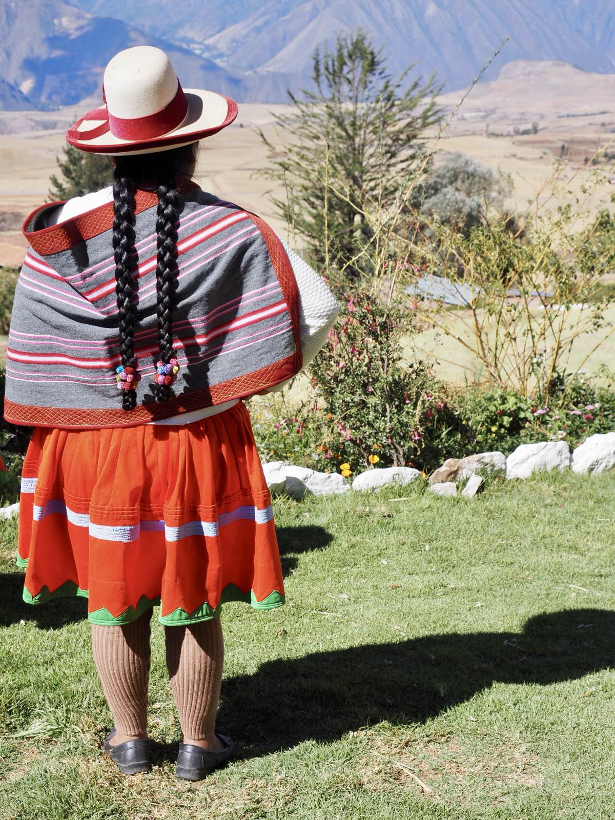 A woman in a traditional hat, shawl, and skirt looking out over the valley