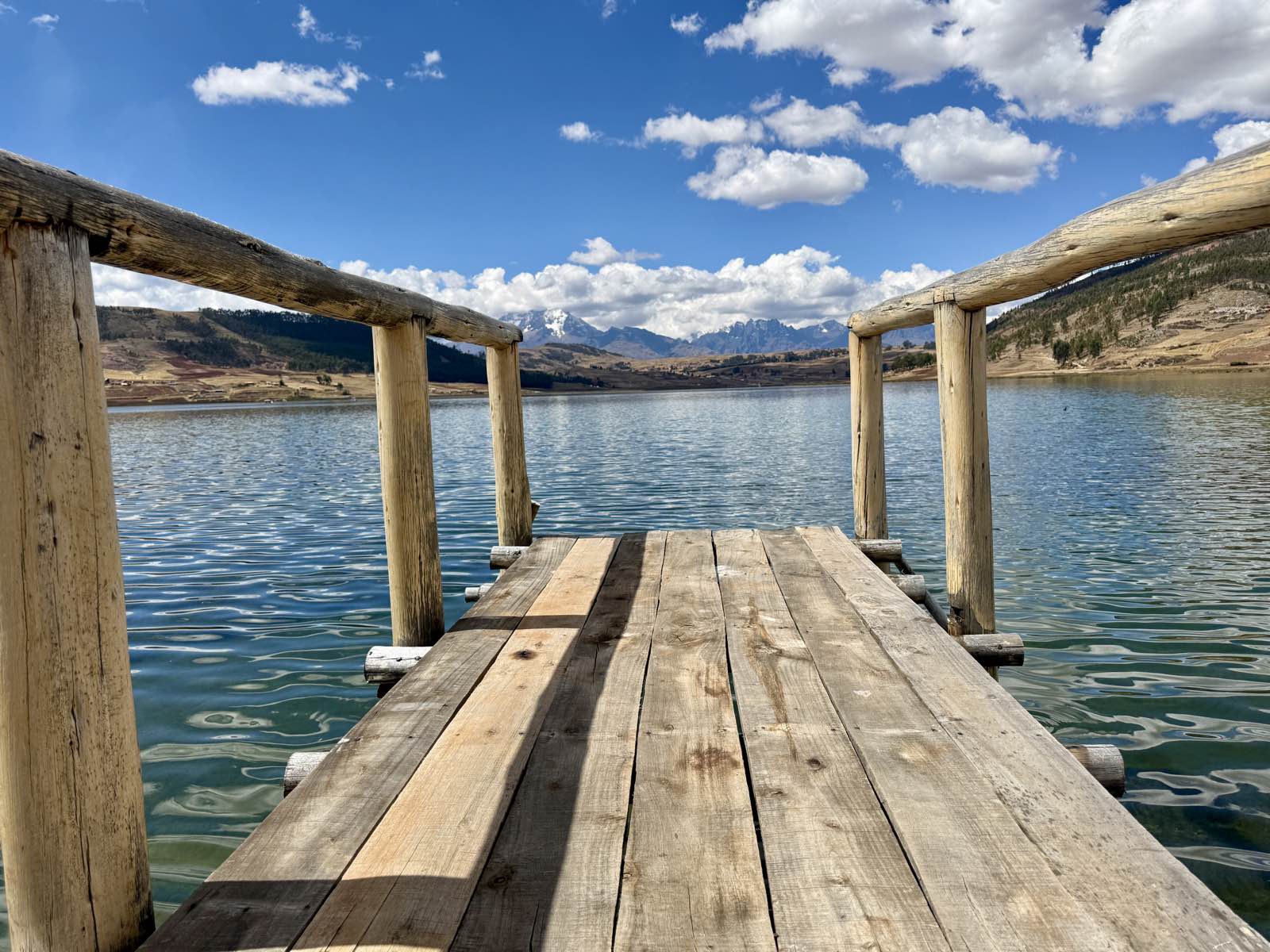 Wooden dock leading out onto a lake with snow-capped Andes in the distance